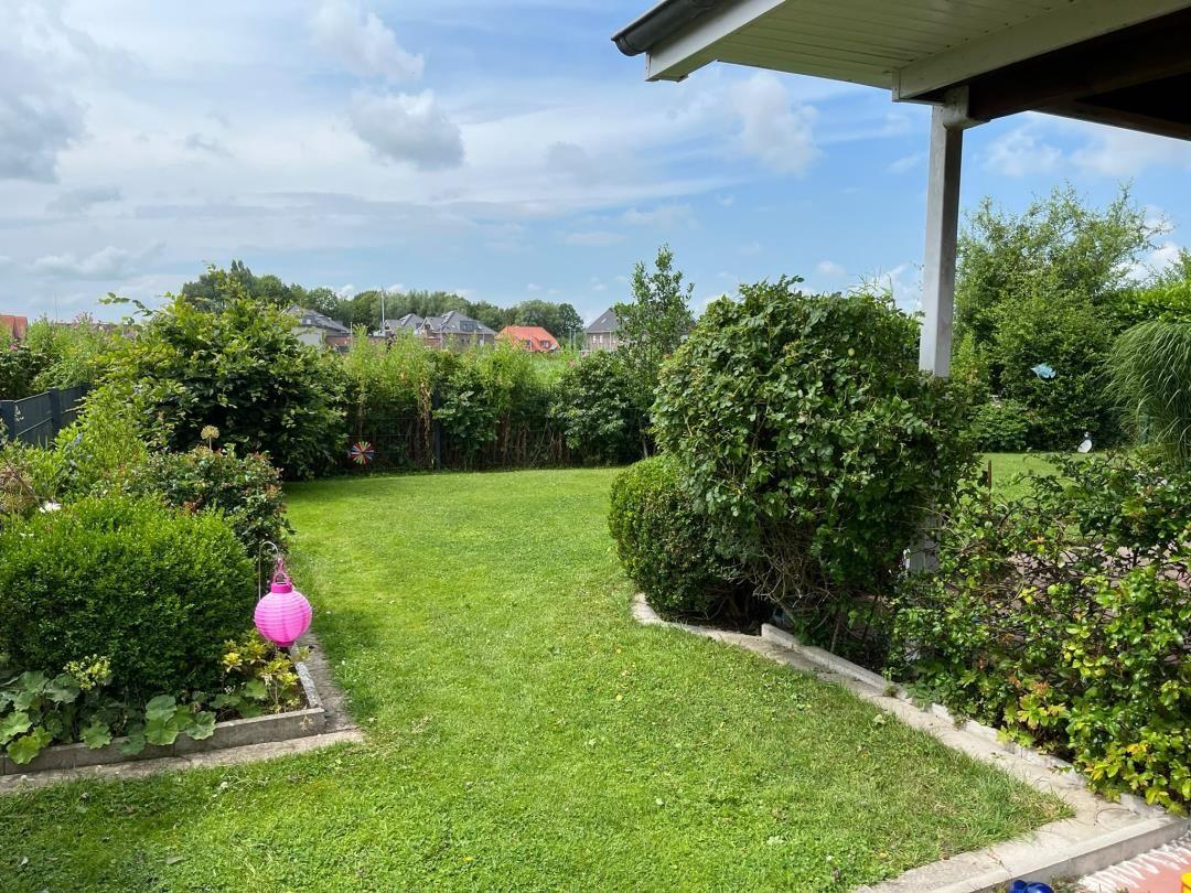Garten mit Rasenfläche, Beete und Sträuchern. Pinker Laterne und Sicht auf Nachbarhäuser.