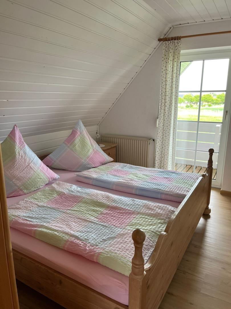 Zimmer mit Doppelbett, Holzboden und Balkontür. Decke mit Holzverkleidung.