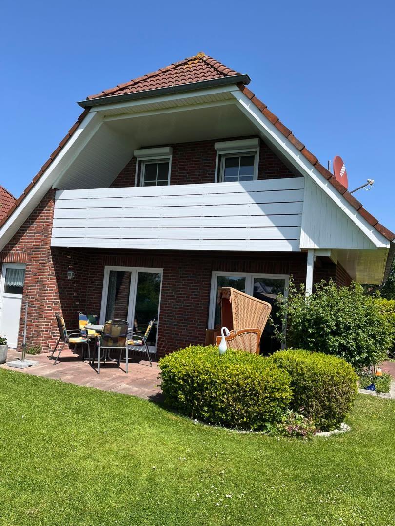 Haus mit Balkon, Terrasse und Garten. Möbel und Pflanzen sind sichtbar.