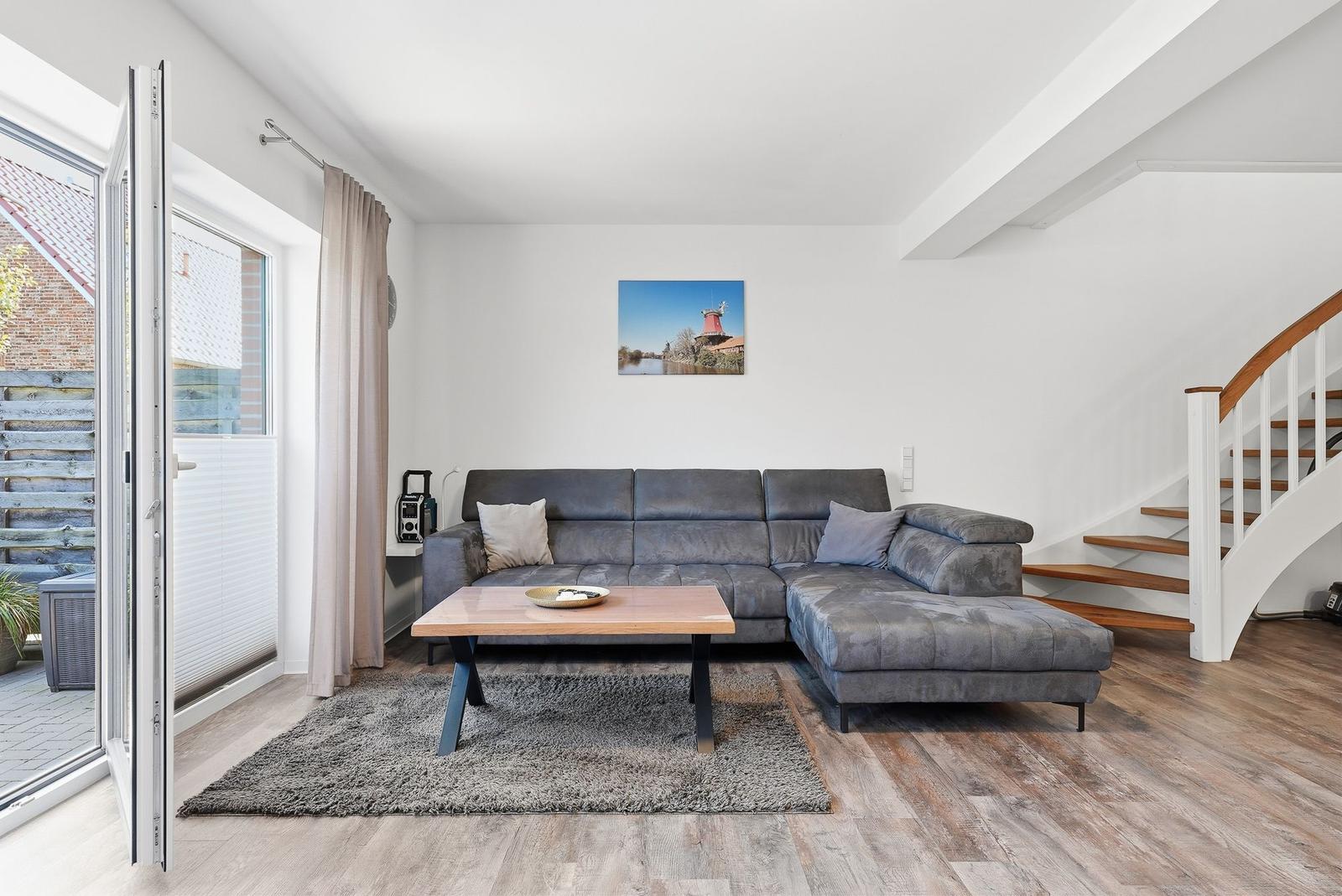 Wohnzimmer mit grauem Sofa, Holztisch und Treppe zur oberen Etage.