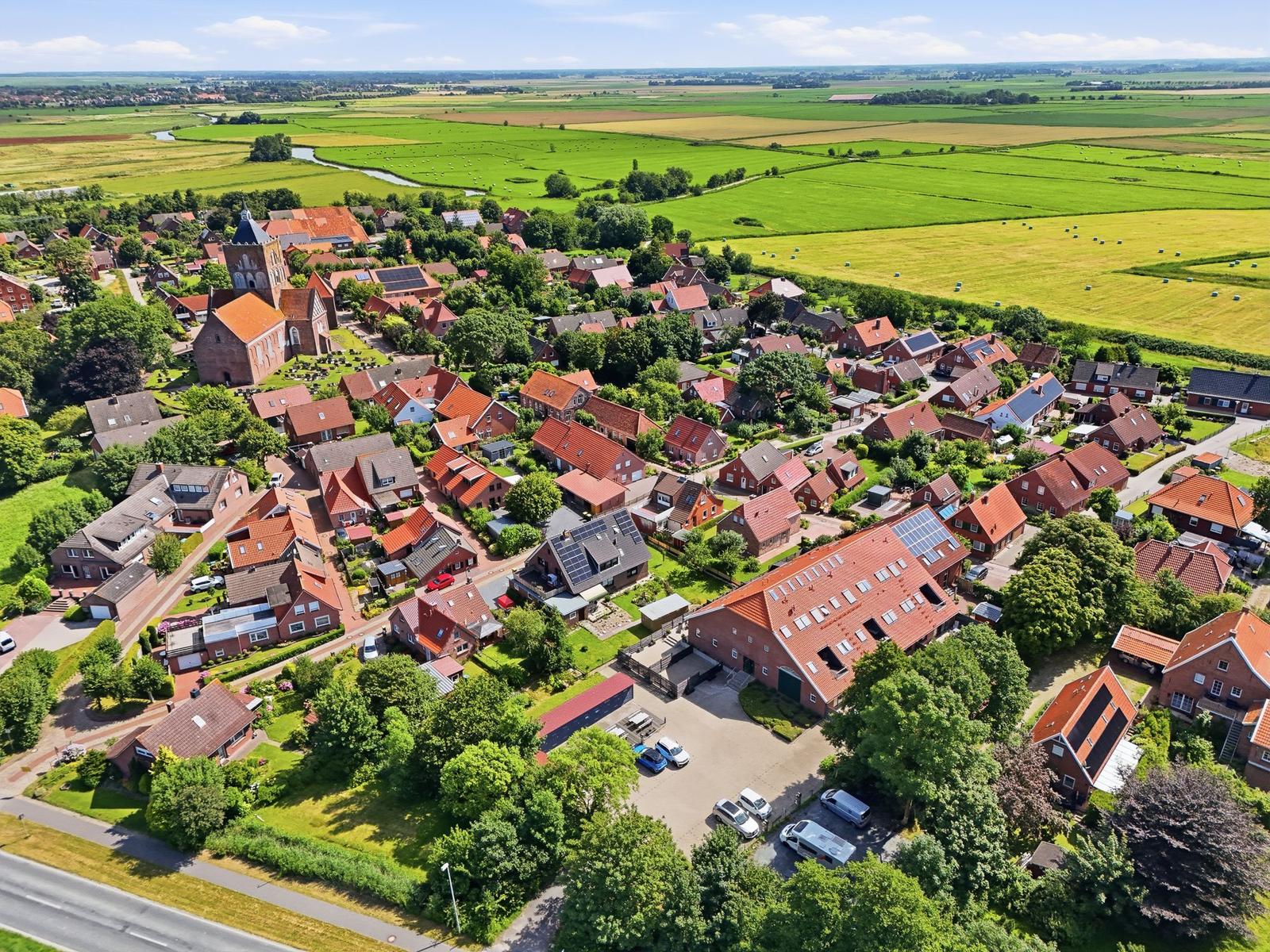 Dorf mit roten Dächern, umgeben von grünen Feldern und einem Fluss.