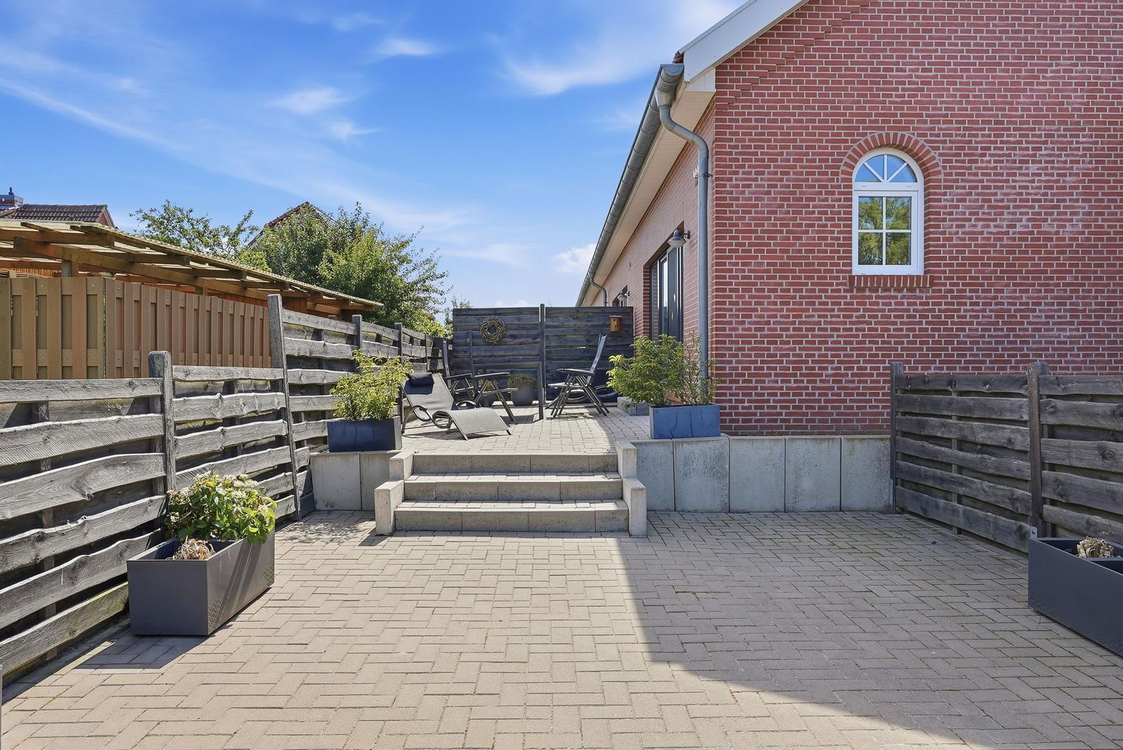 Hinterhof mit Terrasse, Sitzgelegenheiten und Pflanzen vor Backsteinhaus.