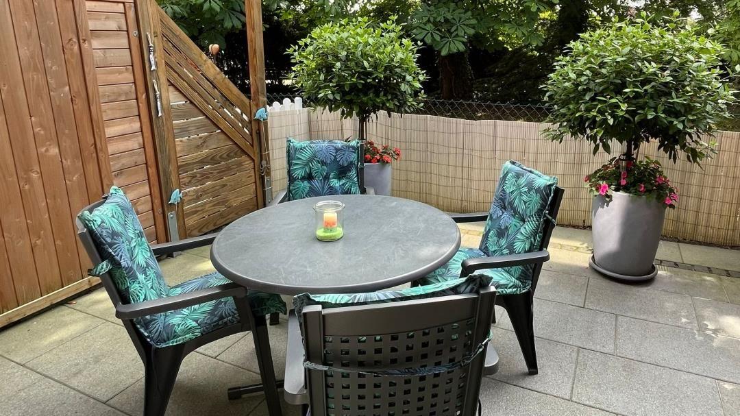 Rundtisch mit vier Stühlen im Garten. Pflanzen und Holzzaun sind sichtbar.