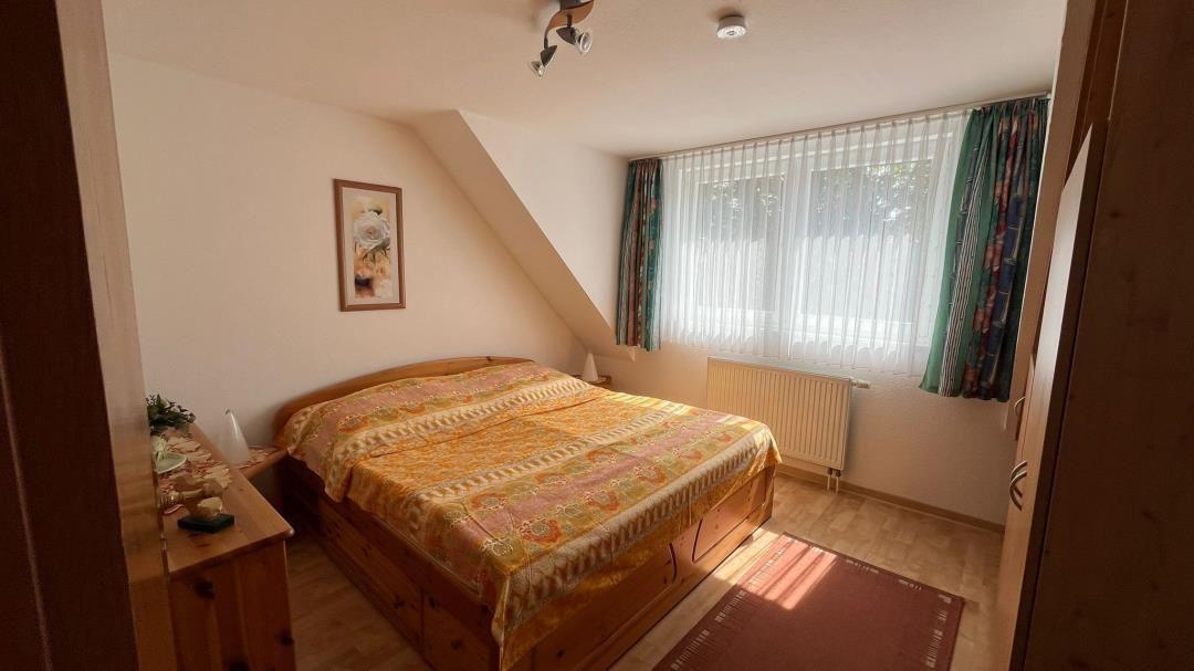 Schlafzimmer mit Dachschrägen, Bett, Fenster mit Vorhängen und Holzmöbel.