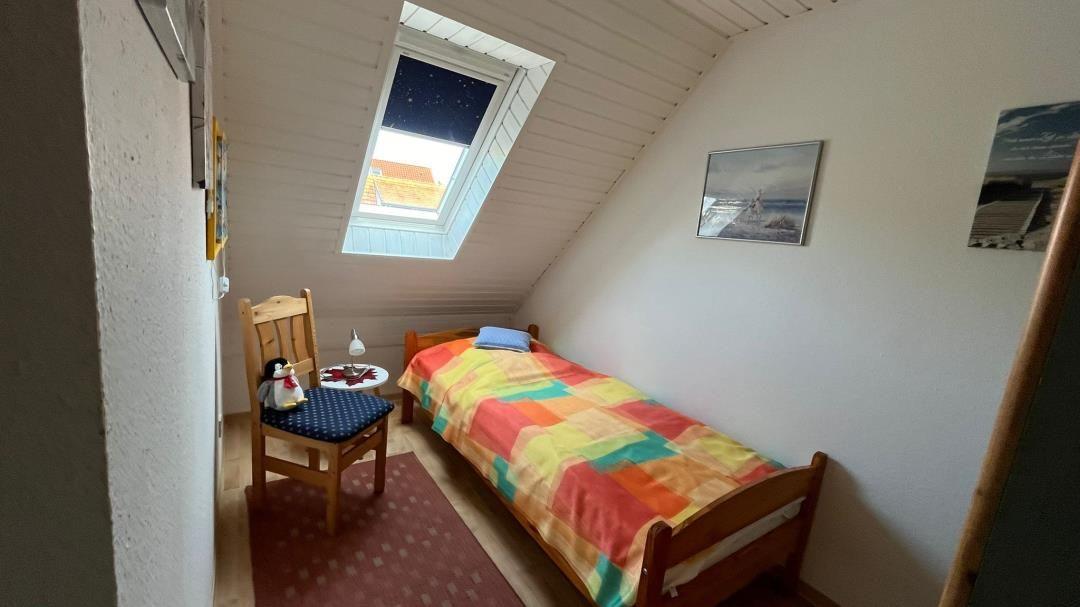 Ein Schlafzimmer mit Dachschrägen, einem Bett und einem Fenster. An der Wand hängen zwei Bilder.
