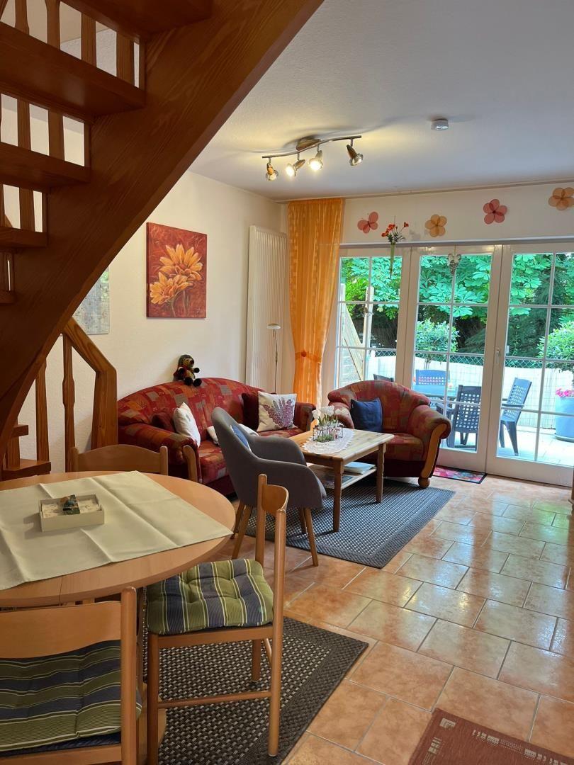 Wohn- und Essbereich mit Holztreppe, Sofa, Stühlen und Blick auf Balkon.