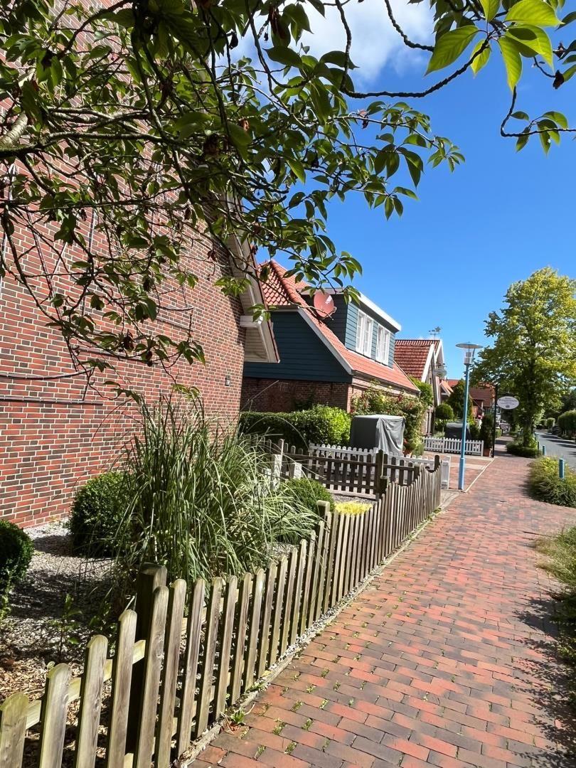 Gepflasterter Weg neben einem Haus mit Holzzaun und grüner Vegetation.