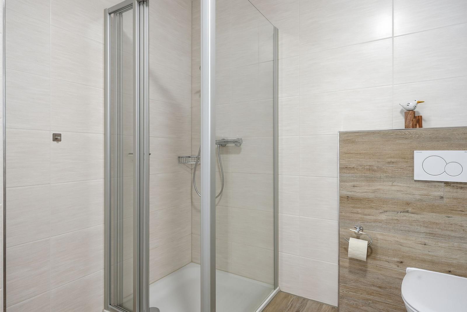 Dusche mit Glaswand, Toilette und Holzverkleidung an der Wand.