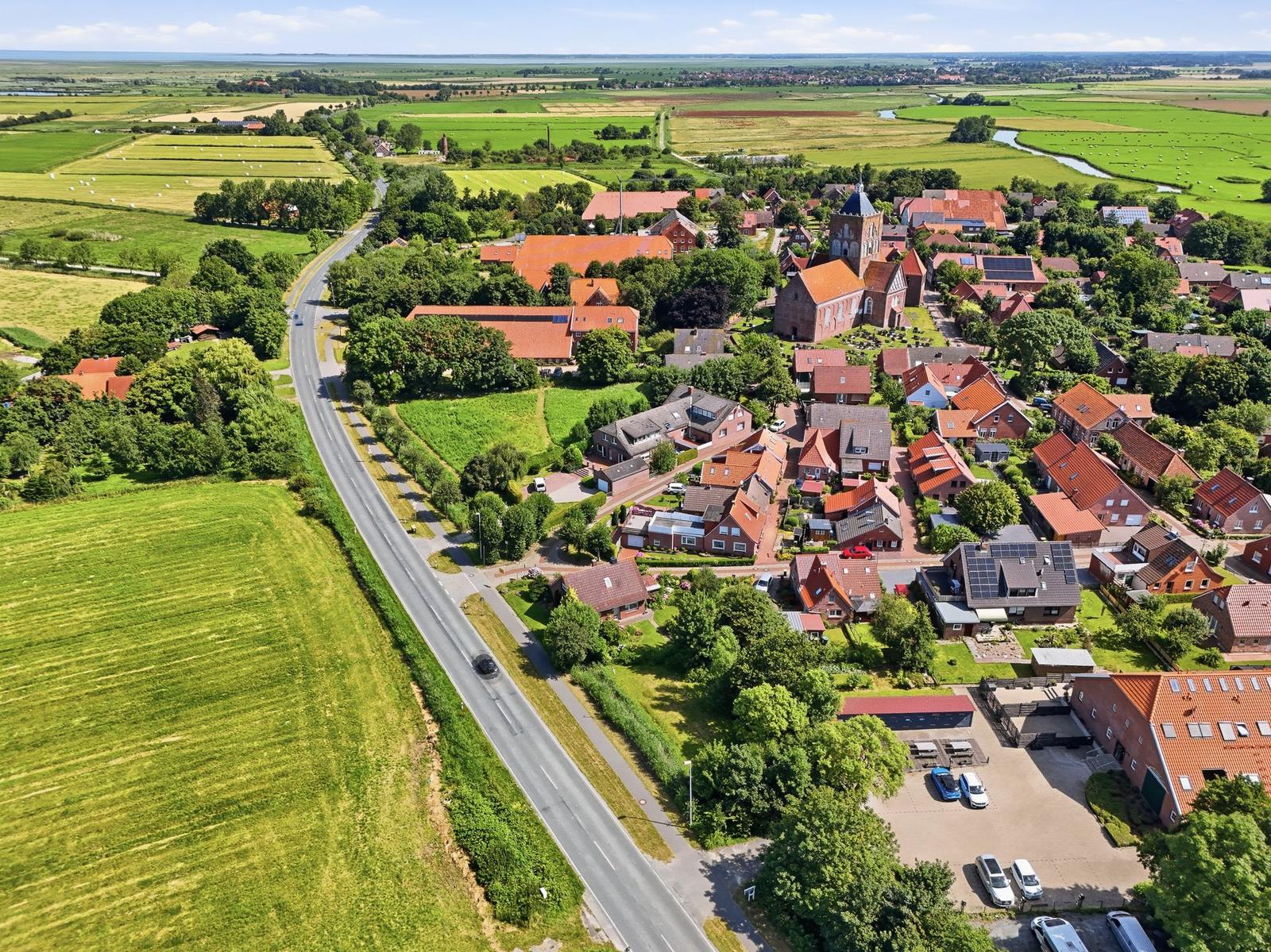 Aerial view of a village with red-roofed houses, green fields, and a road running through.