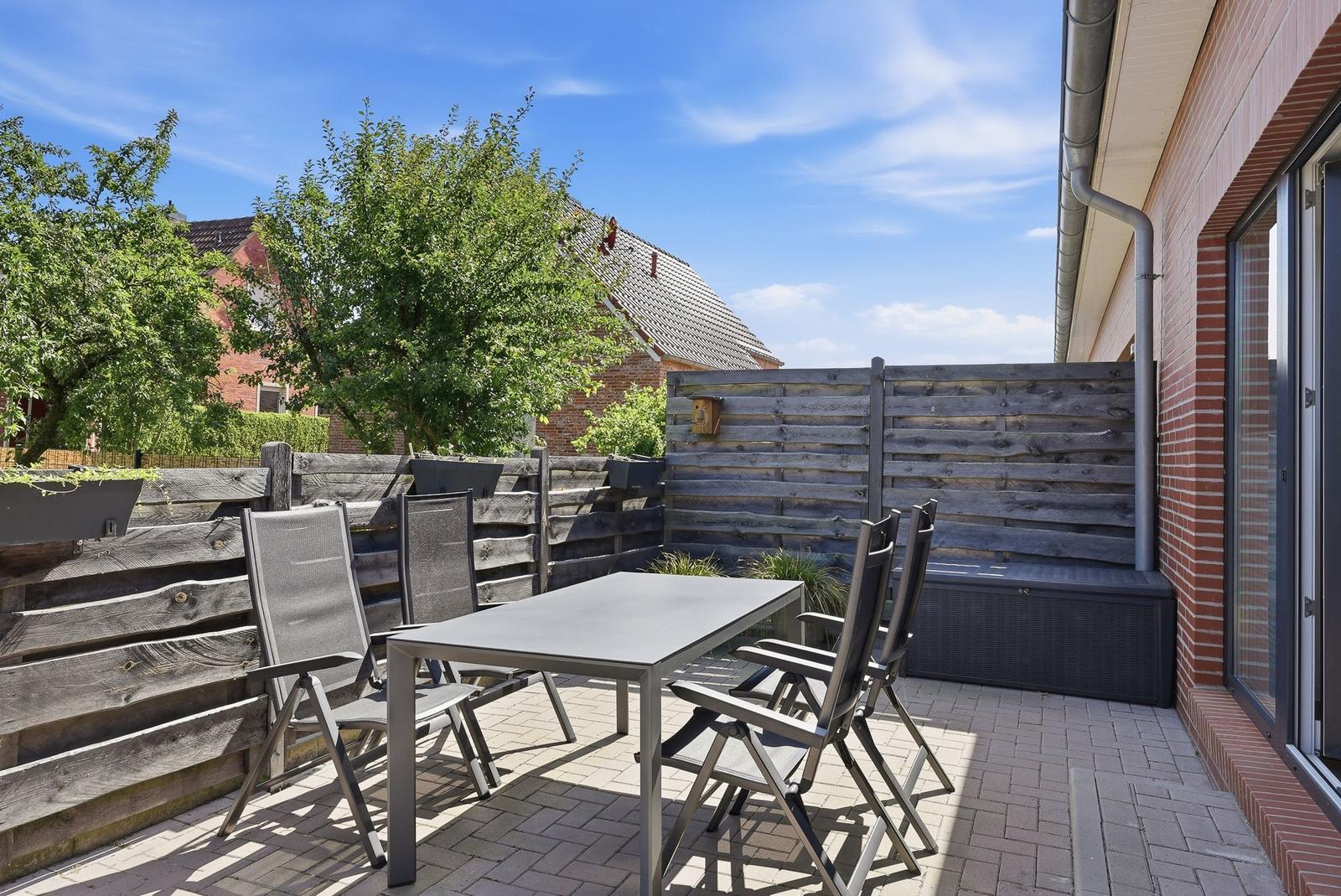 Terrasse mit Tisch und Stühlen, Holzzaun und Blick auf Nachbarhaus.