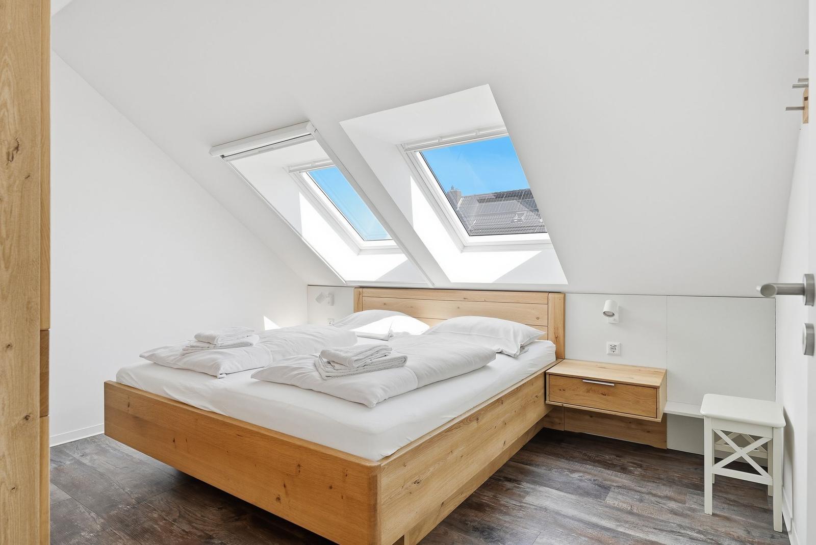 Schlafzimmer mit Dachfenstern, Holzbett und Nachttisch.