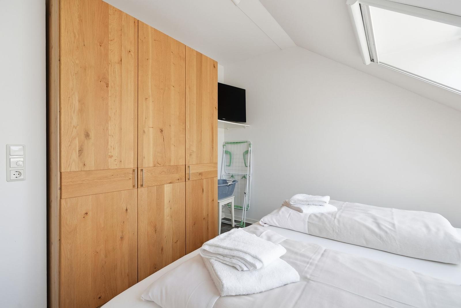 Schlafzimmer mit Dachschrägen, Holzschrank und Dachfenster. Bett mit weißen Laken und Handtüchern.