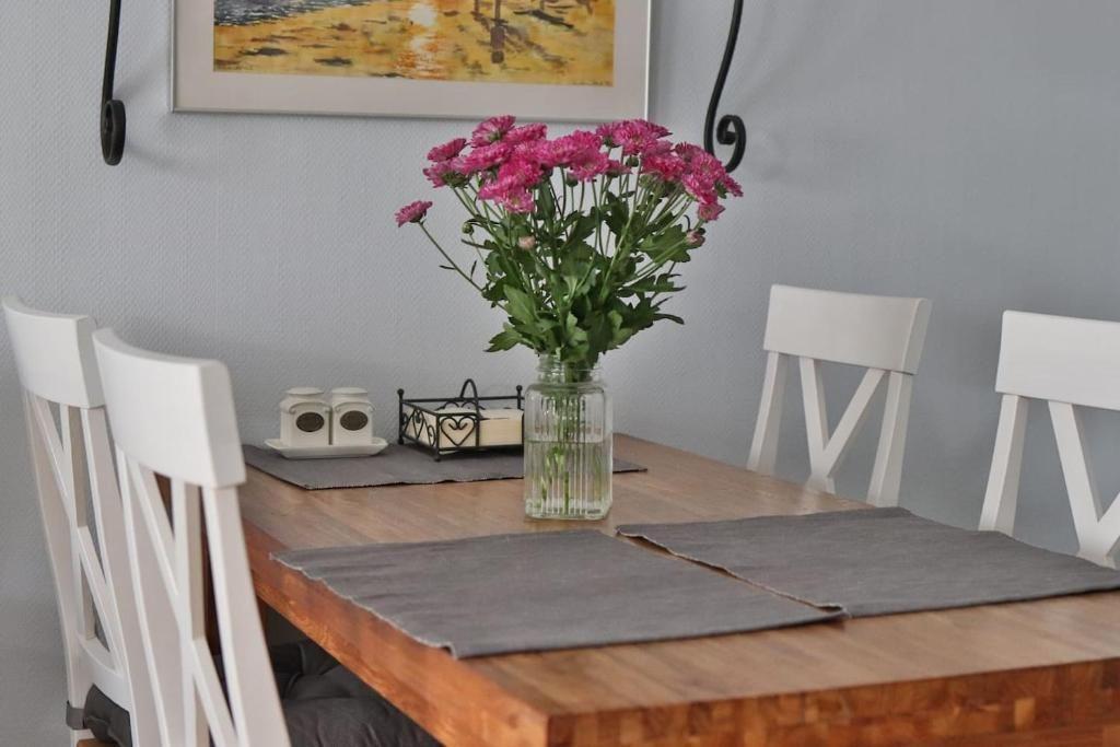 Holztisch mit weißen Stühlen, Blumen in Glas und Platzsets.