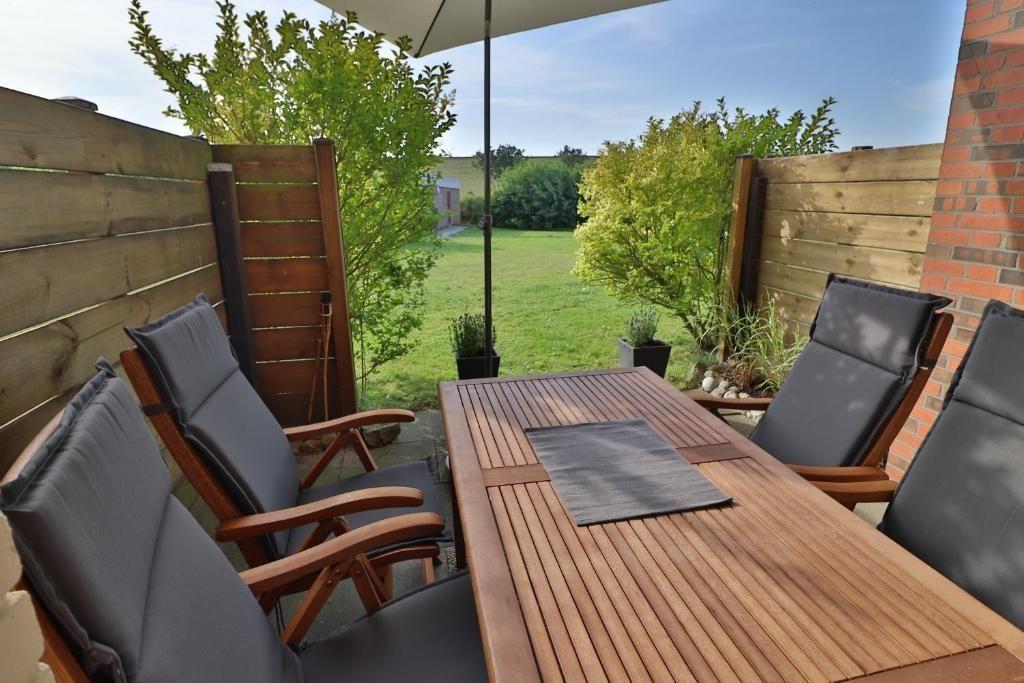Terrasse mit Holztisch, vier Stühlen und Sonnenschutz. Hinterhof mit Rasen und Bäumen.