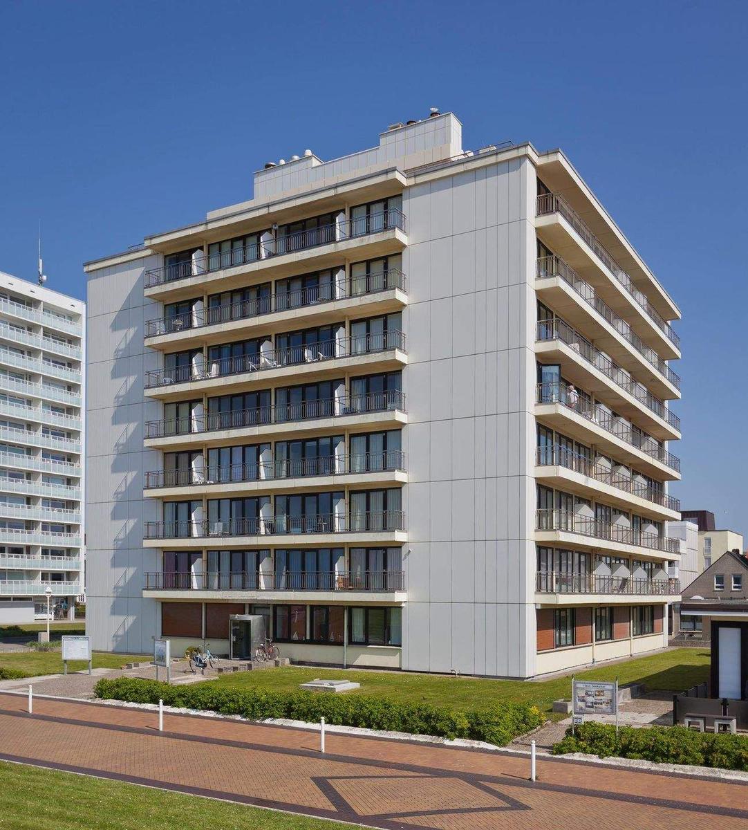 Hochhaus mit Balkonen und Fenstern, umgeben von Grünflächen und einem Gehweg.