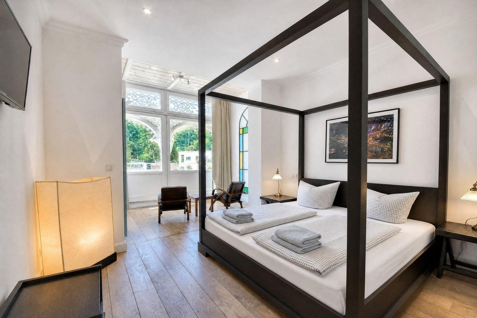 Schlafzimmer mit vierbettkonstruktion, Holzboden und Blick auf Balkon