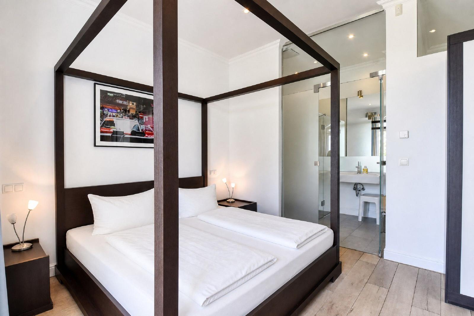 Schlafzimmer mit Doppelbett, Nachttischen und Glaswand zum Bad