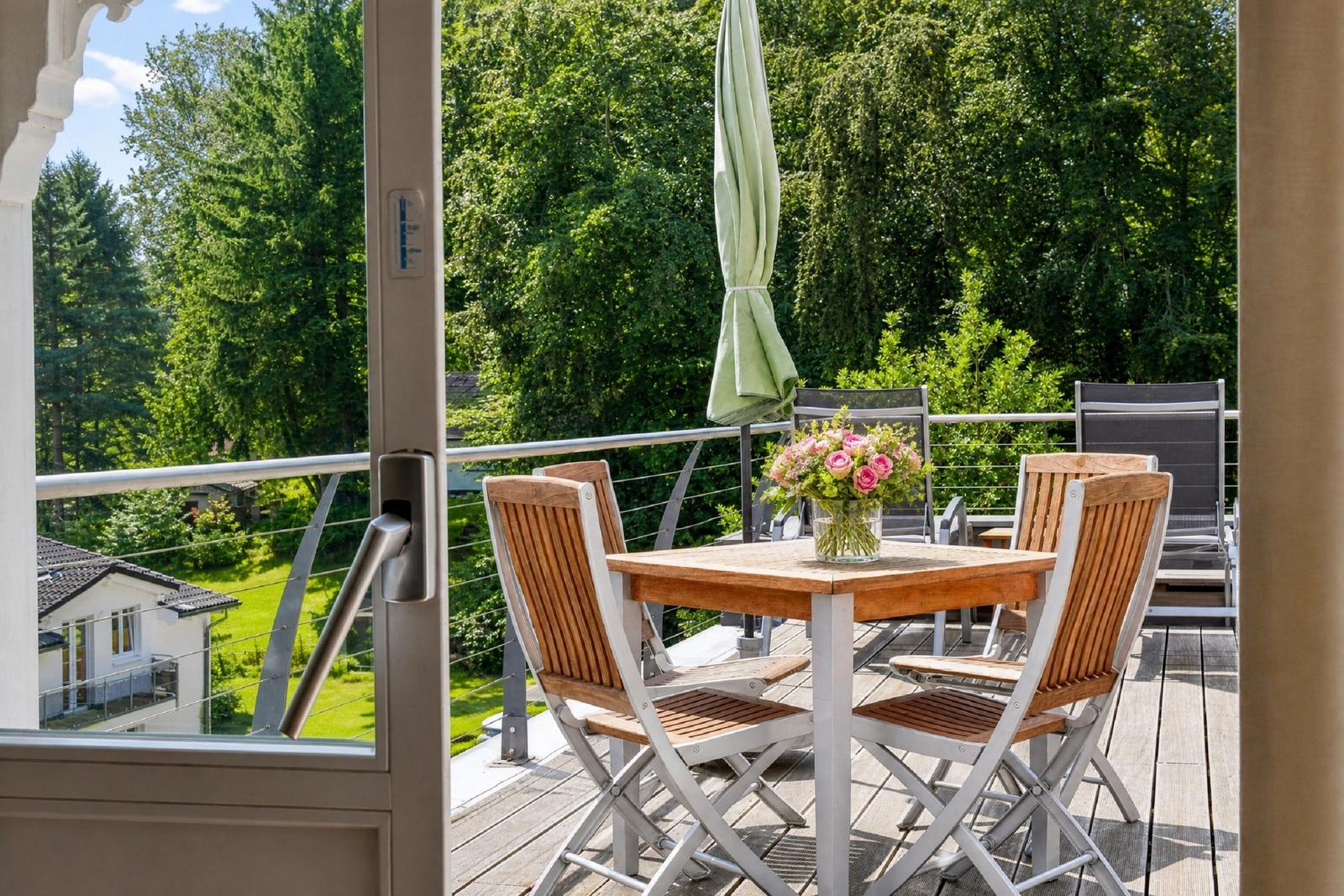 Terrasse mit Tisch, Stühlen und Blumen, Blick in grüne Landschaft.