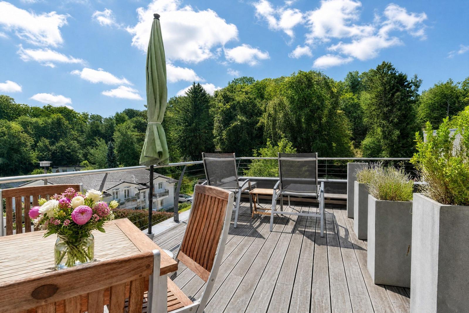Terrasse mit Tisch, Stühlen und Blick auf grüne Bäume.