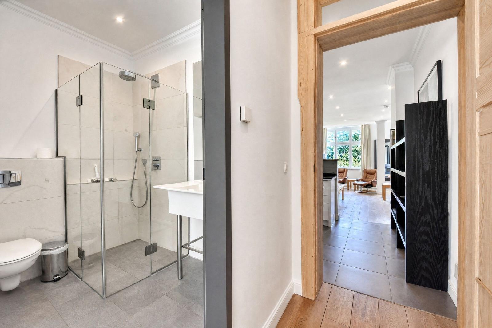 Badezimmer mit Dusche und Waschbecken. Durchgang in Wohnbereich mit Holzrahmen.