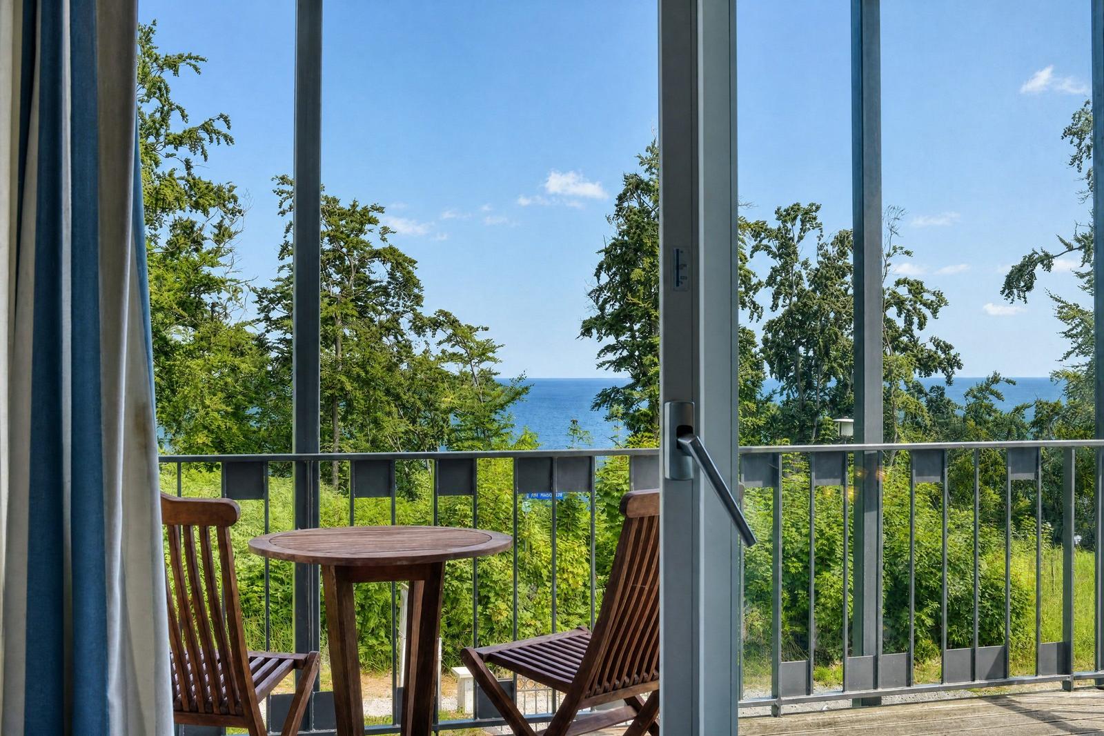 Terrasse mit Tisch und Stühlen, Blick auf Wald und Meer.
