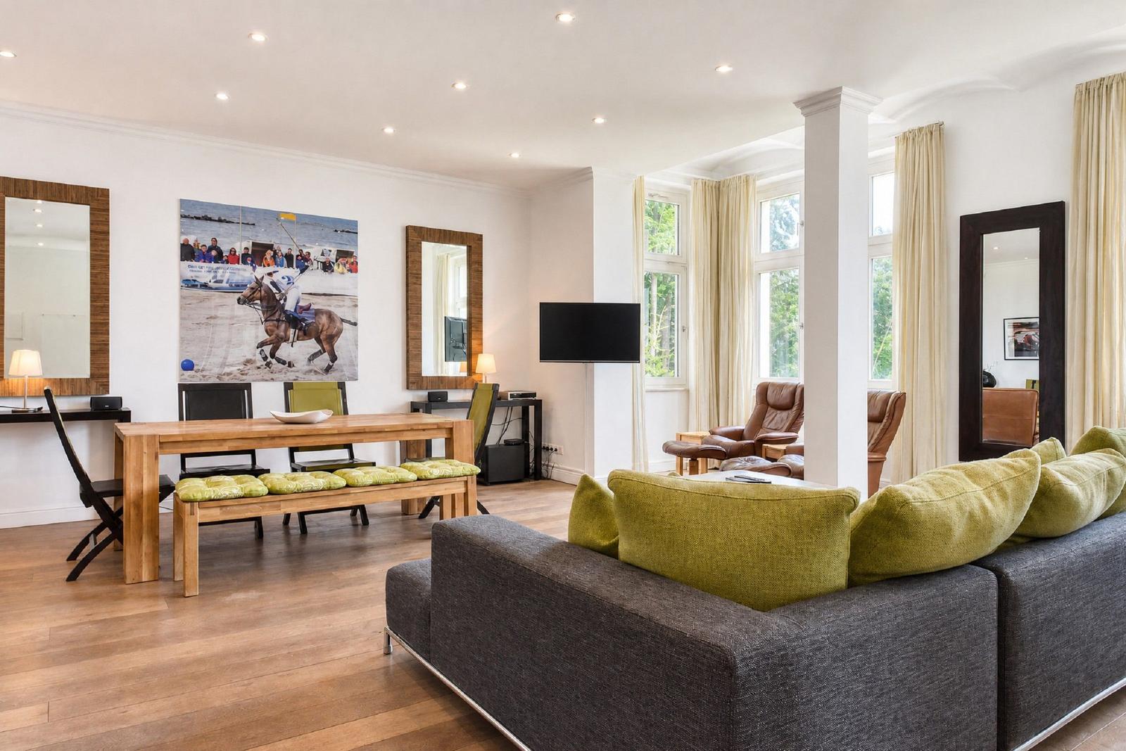 Wohnbereich mit Sofa, Esstisch und Wandbild. Holzboden und große Fenster.