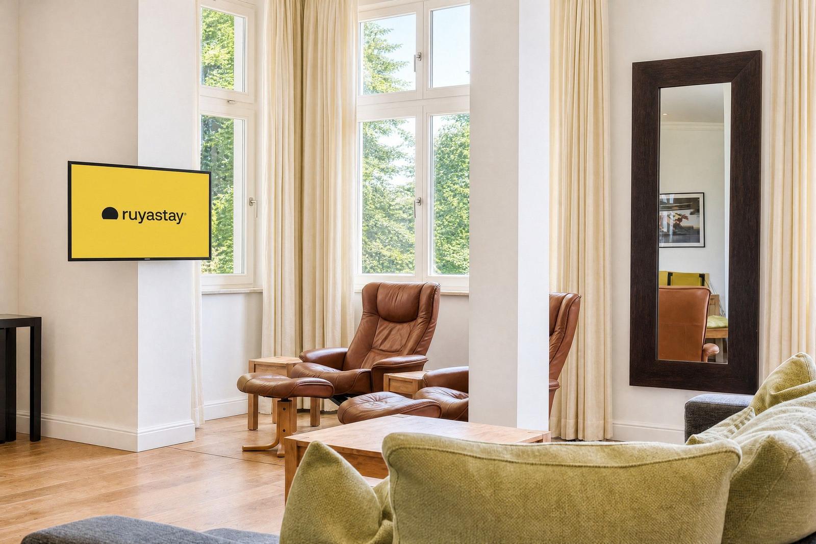 Wohnzimmer mit braunen Sesseln, Holztisch und Fernseher an der Wand.