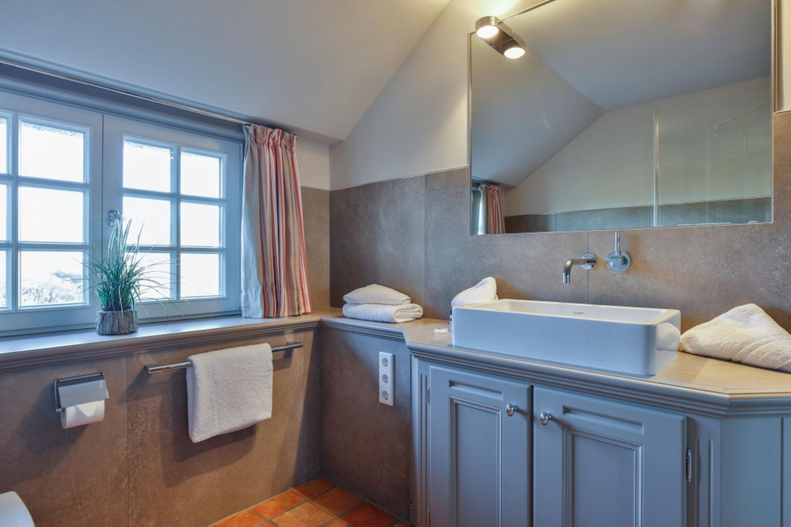 Badezimmer mit Waschbecken, Spiegel, Fenster und Handtüchern.