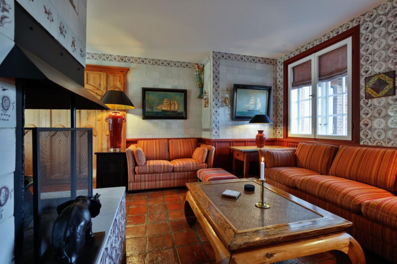 Wohnzimmer mit Sofa, Kamin und Terrakottaboden. Wandgestaltung mit Tapeten und Bildern.