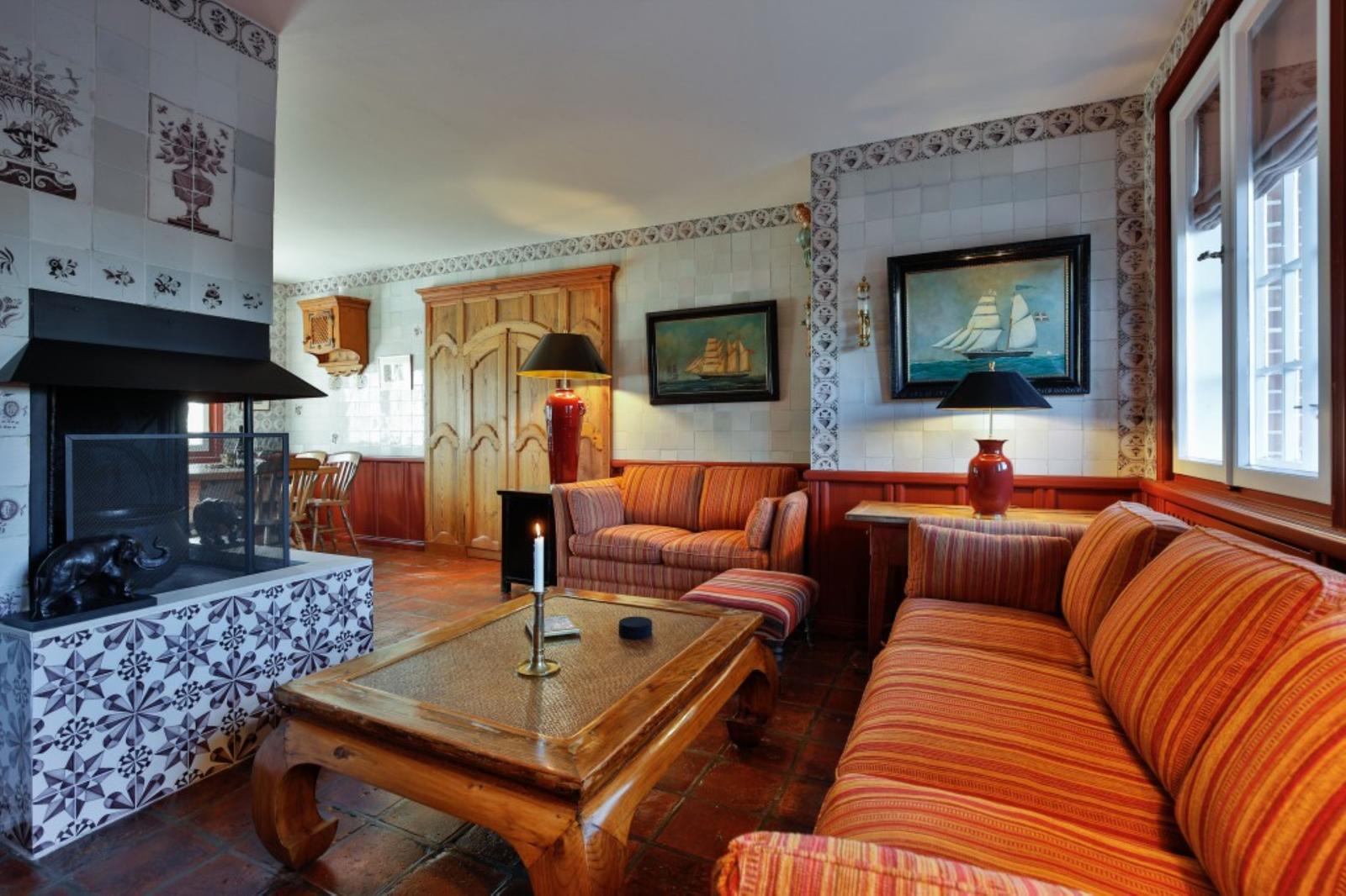 Wohnzimmer mit Kamin, Sofa und Holztisch. Wandfliesen und Gemälde sichtbar.