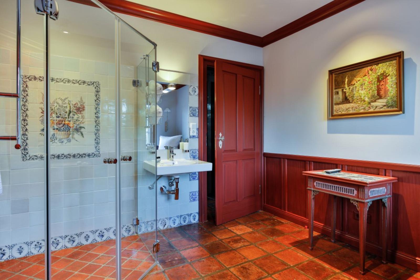Badezimmer mit Dusche, Waschbecken und Holztisch. Terrakottafußboden und rote Holzverkleidung.