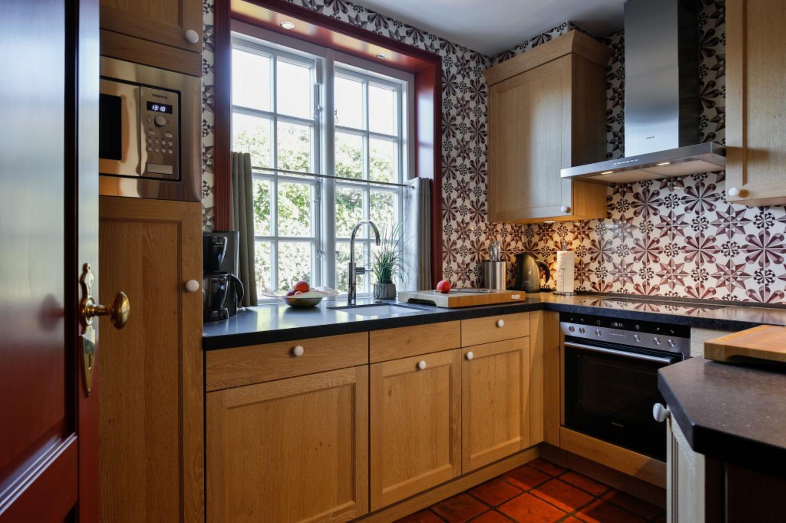Küche mit Holzschränken, Fenster, Spüle und Backofen.