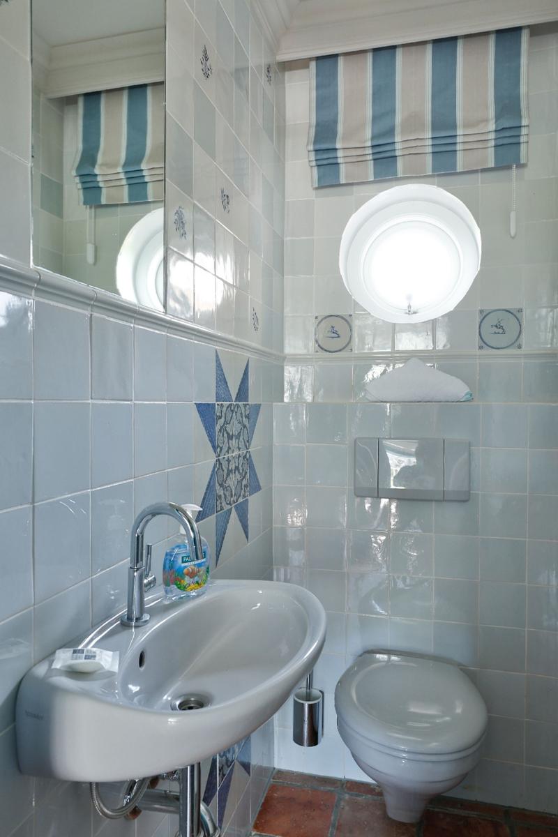 Badezimmer mit Waschbecken, Toilette und runden Fenster. Wandfliesen mit blauem Muster.
