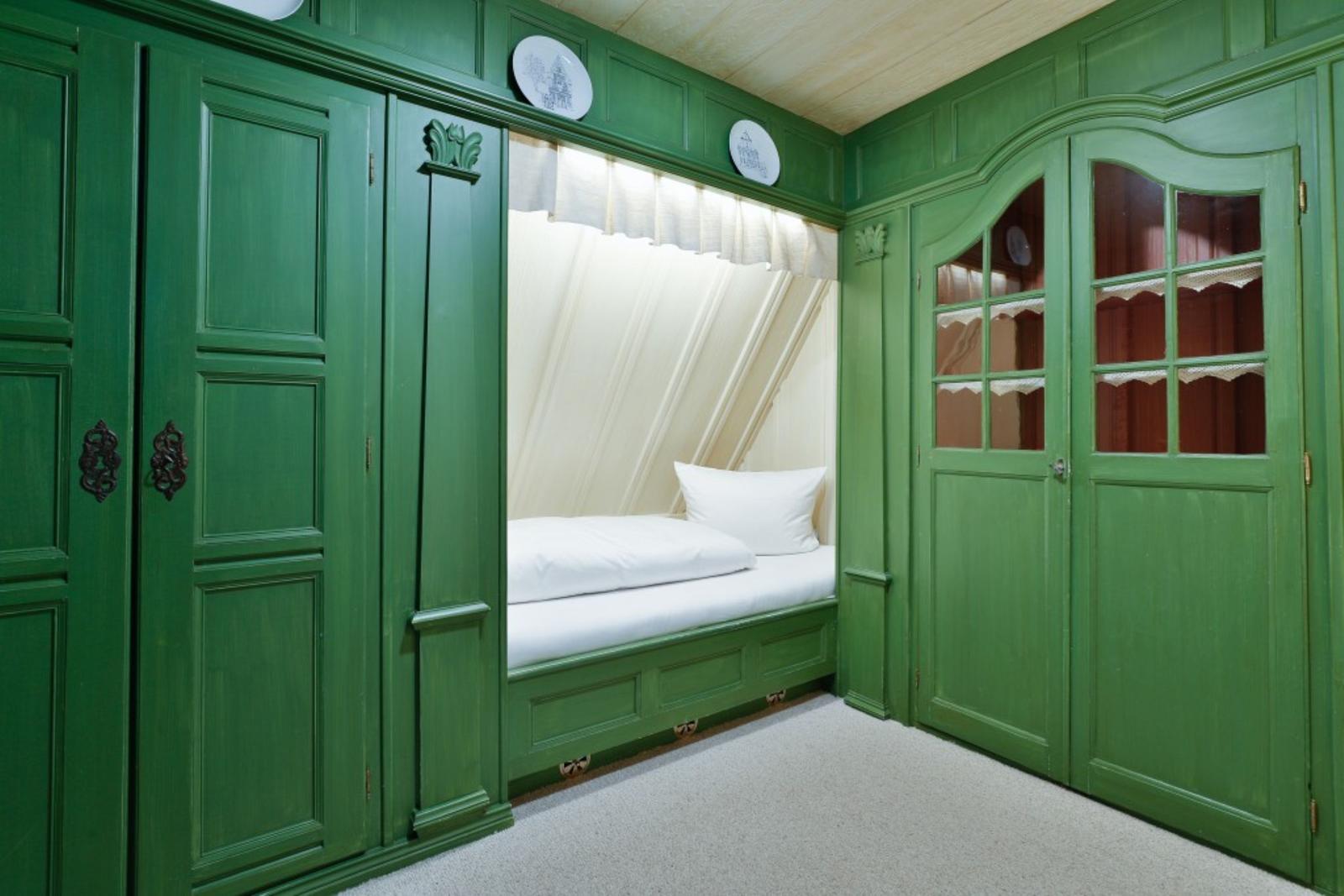 Ein Bett in einem grünen Schrank mit Vorhängen und Holzwandverkleidung.