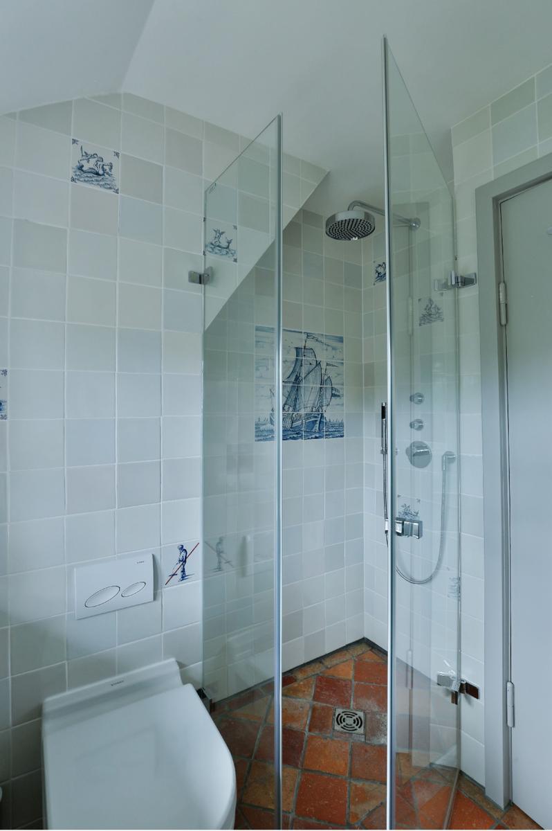 Dusche mit Glaswand, Toilette und Wandfliesen mit Segelyacht-Motiven.
