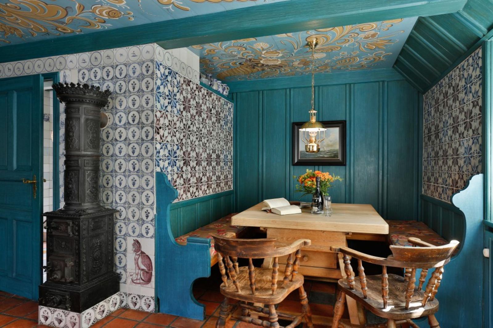 Esszimmer mit Holztisch, Stühlen und dekorativen Wandfliesen. Decke mit goldenen Mustern.