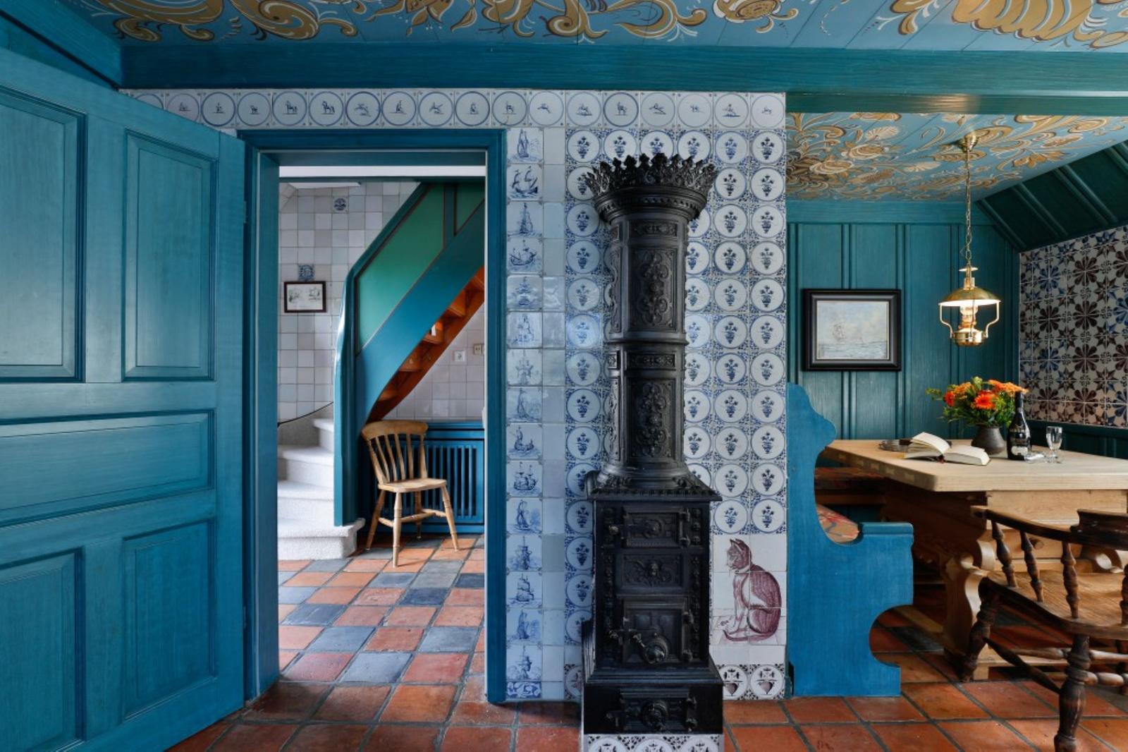 Raum mit blauen Wänden, Ziegelboden und Zentralheizung. Durchgang zu Treppenhaus mit Holzstuhl.