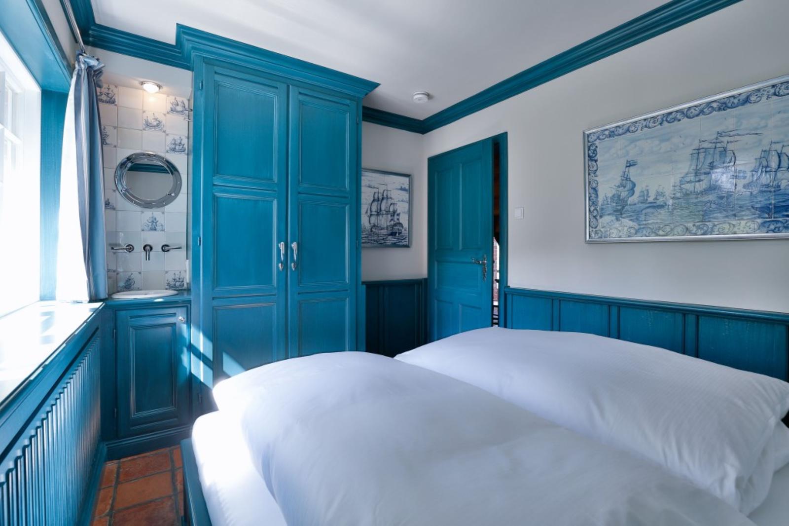 Schlafzimmer mit blauem Schrank, Bett und Wandbildern mit Schiffen.