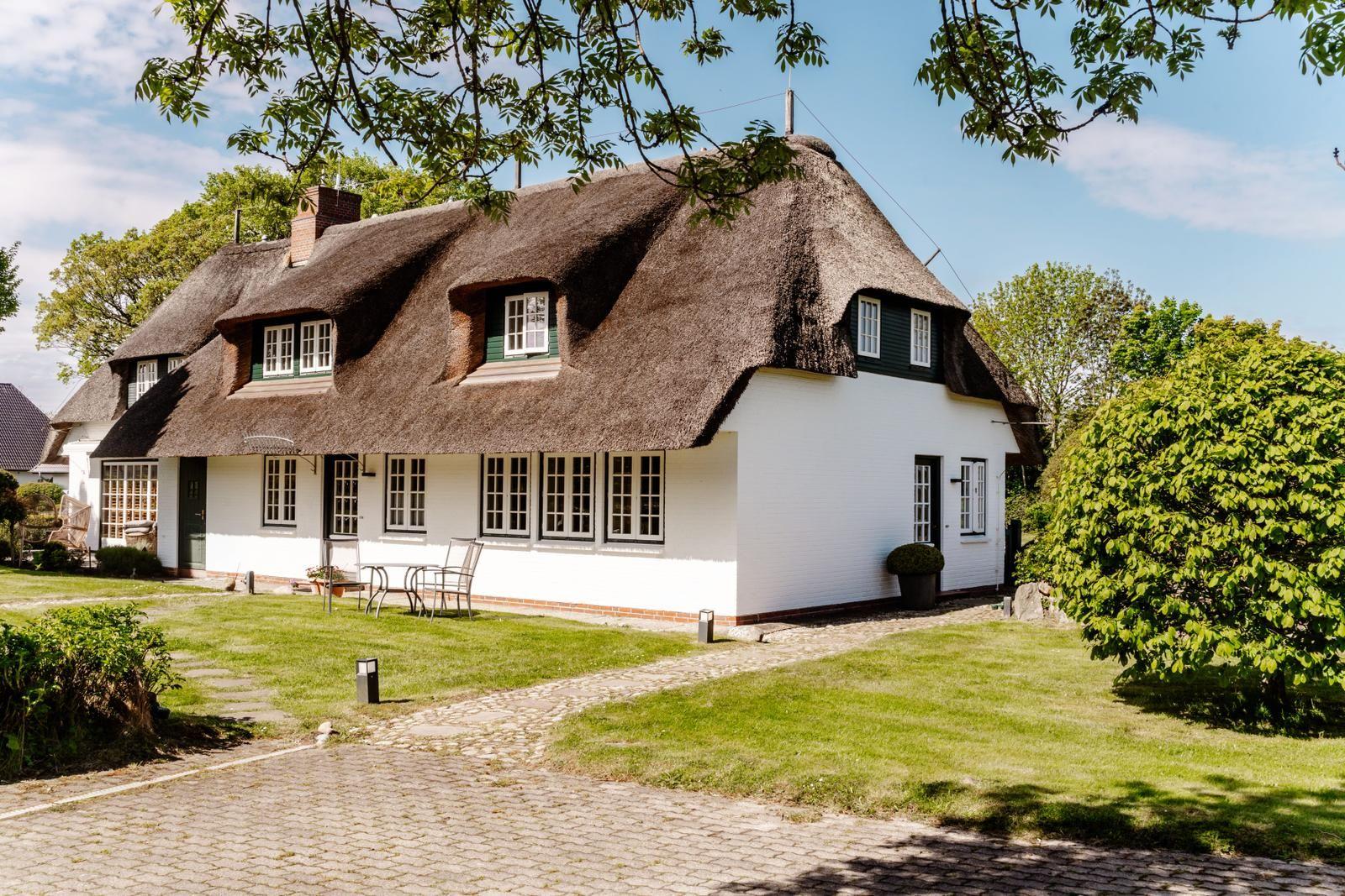 Ein weißes Haus mit Strohdach, Fenstern und einer Terrasse im Garten.