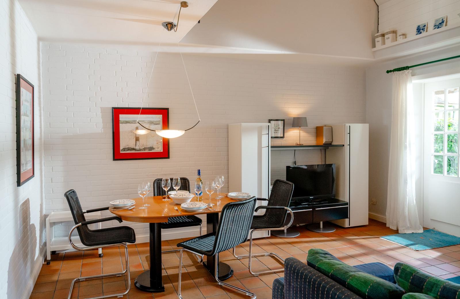Essbereich mit Tisch, Stühlen und Fernseher. Weiße Ziegelwand und Terrakottaboden.