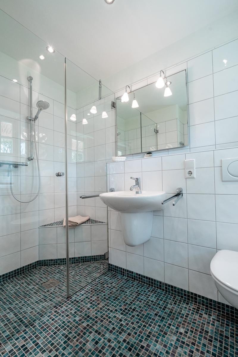 Badezimmer mit Dusche, Waschbecken und Toilette. Bodenfliesen in Blautönen.