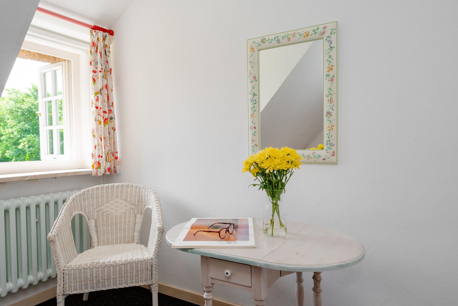 Ein Raum mit Stuhl, Tisch, Blumen und Spiegel an der Wand.