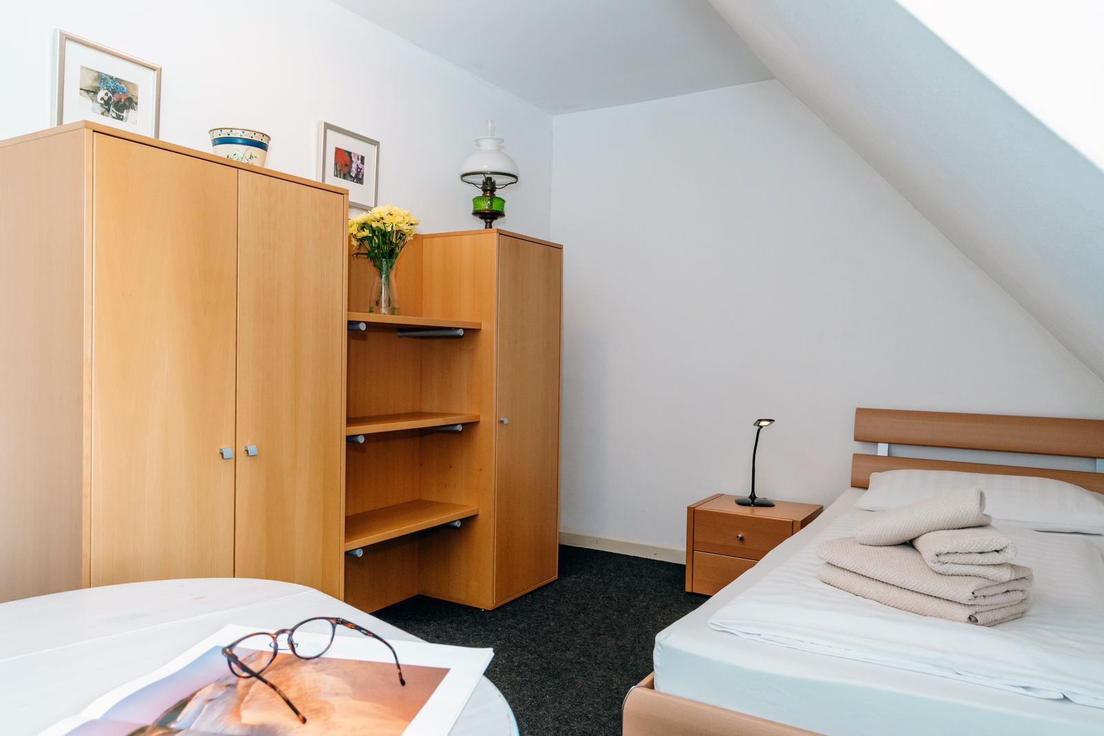 Schlafzimmer mit Dachschräge, Bett, Nachttisch, Kleiderschrank und Blumen.