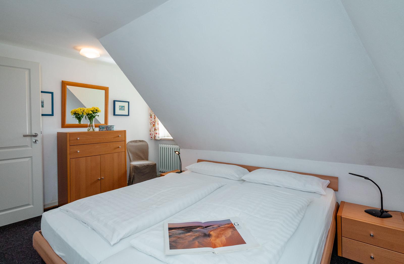 Schlafzimmer mit Dachschräge, Bett, Nachttisch und Schrank.