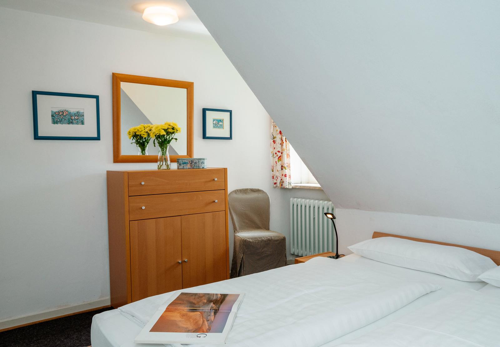 Schlafzimmer mit Dachschräge, Bett, Schrank, Spiegel und Blumen.