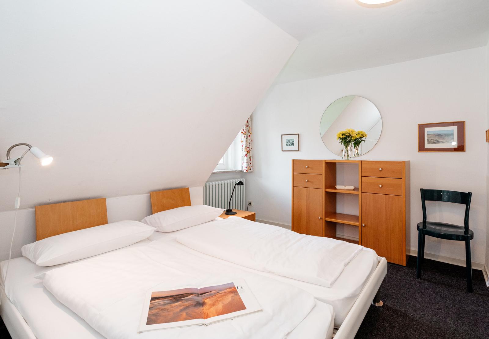 Zimmer mit Doppelbett, Schrank, Stuhl und Spiegel an der Wand.