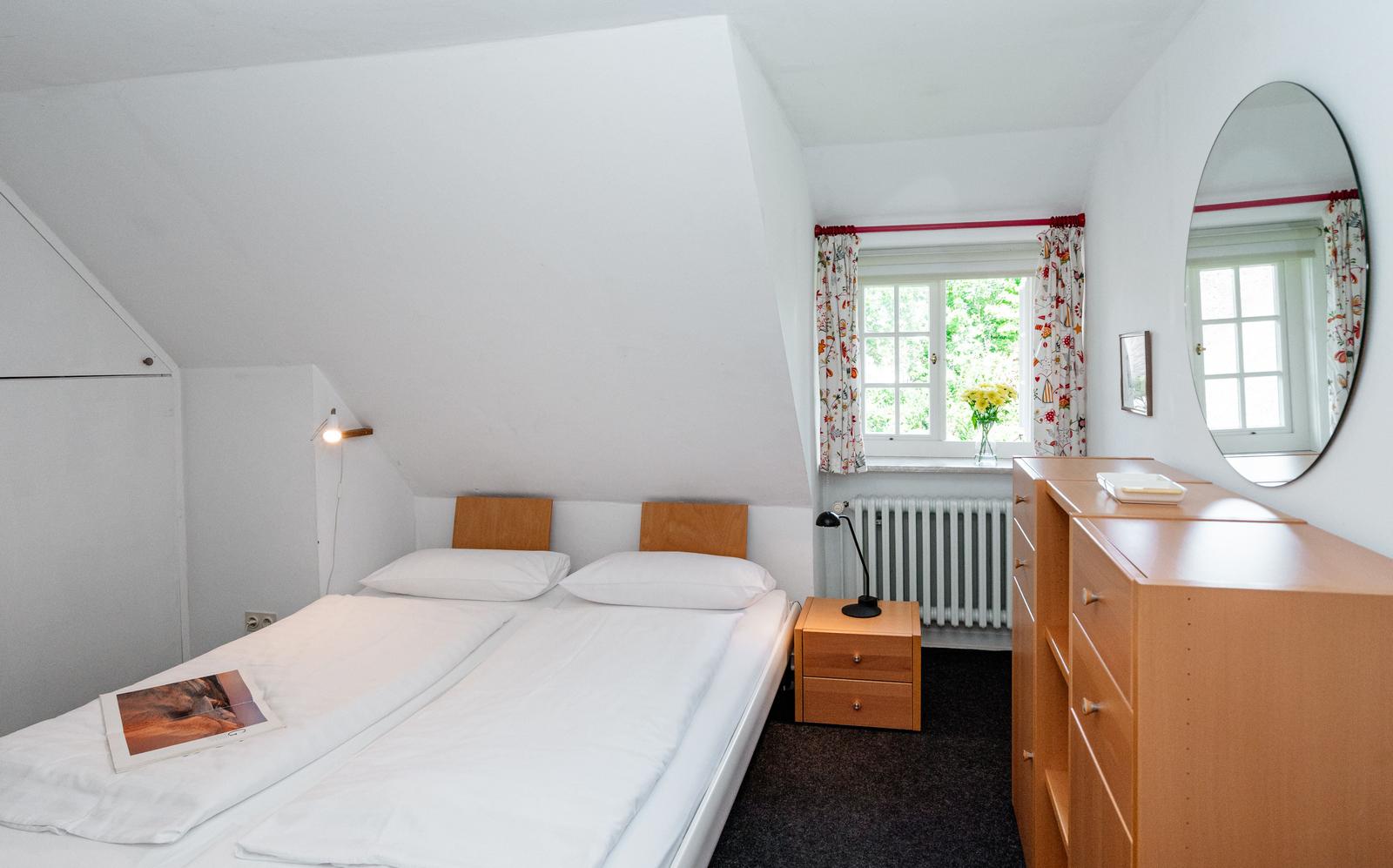 Schlafzimmer mit Doppelbett, Schrank und Fenster mit Blumen.
