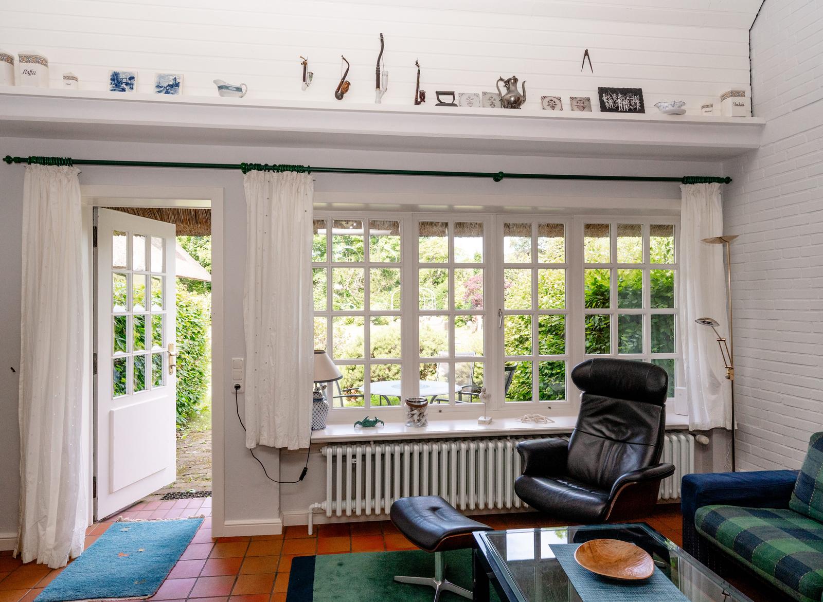 Ein Wohnzimmer mit Blick auf Garten, schwarzer Ledersessel und Glas-Tisch.