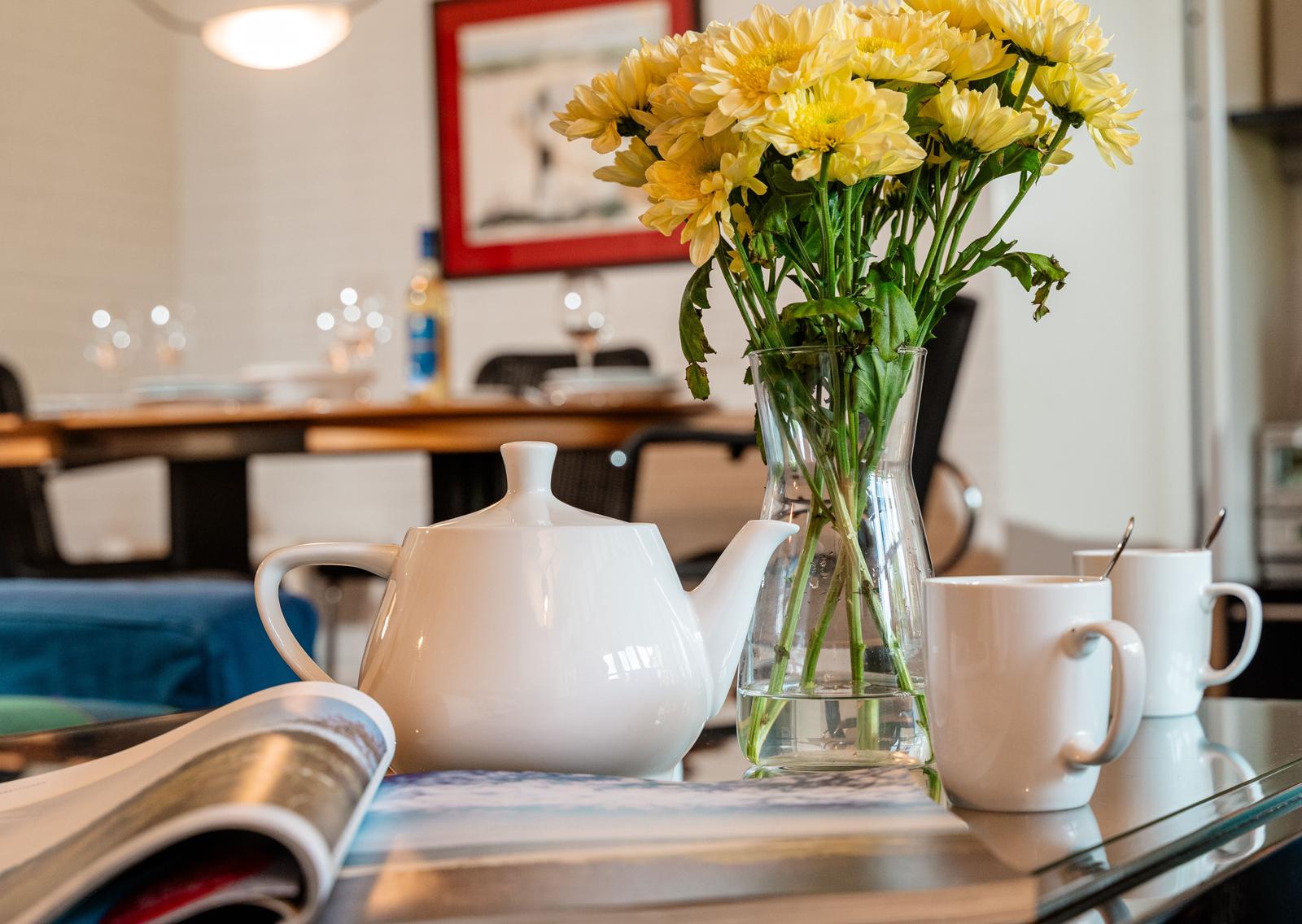 Auf dem Tisch steht eine Teekanne, zwei Tassen und ein Blumenstrauß in einem Glasvasen.