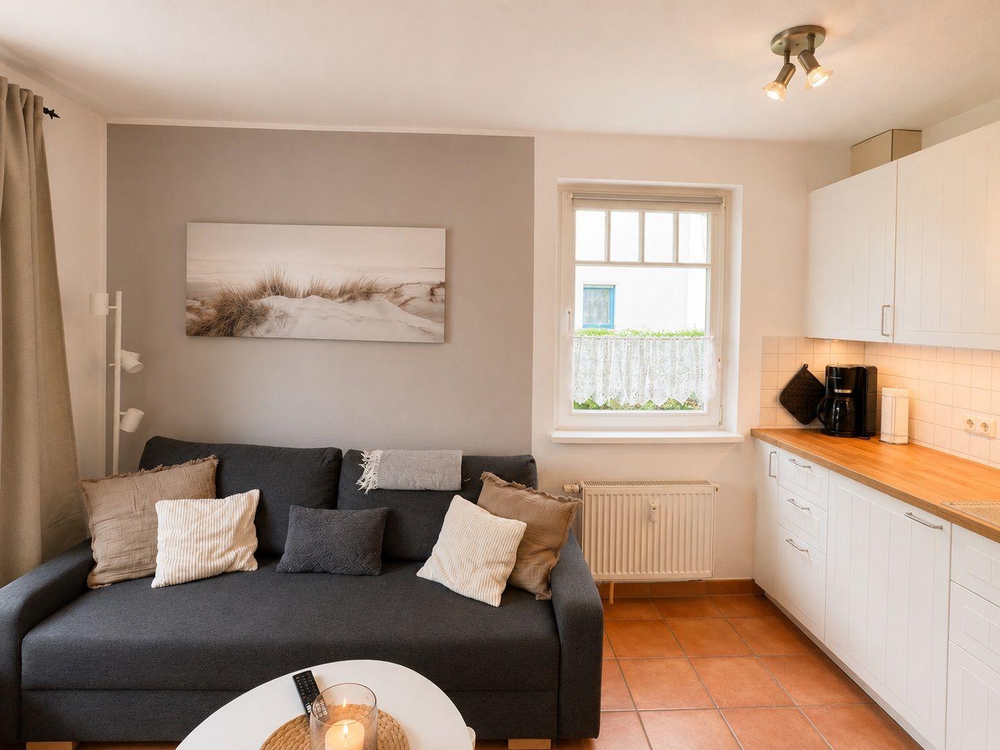 Ein Wohnzimmer mit Sofa, Küchenzeile und Fenster mit Blick nach draußen.